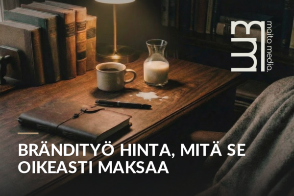Puupöydällä kahvikuppi, maitokannu, muistikirja ja kynä lämpimän lampun valossa