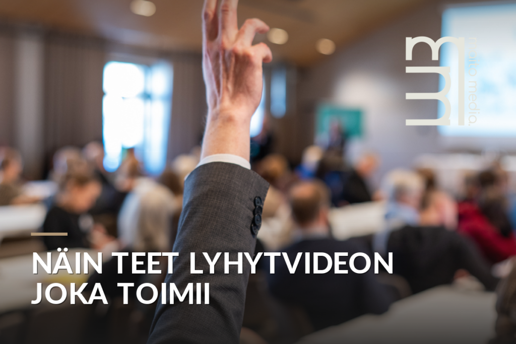 Miehen käsi nousee ylös esityksen tai koulutustilaisuuden aikana puhujien edessä istuvalle yleisölle