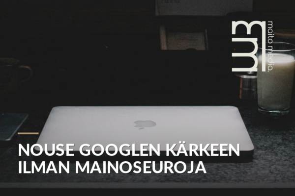 Kannettava tietokone ja kahvikuppi työpöydällä, taustalla toimistoympäristö